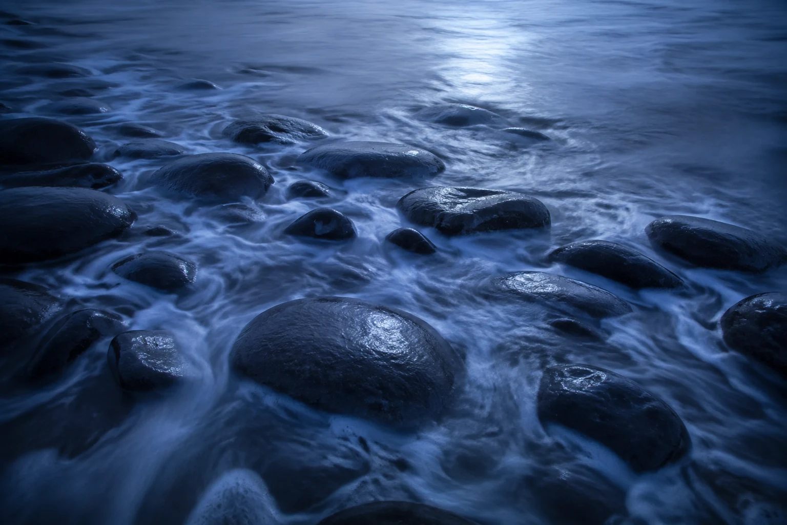 Silver water and soft sea foam flowing around smooth dark stones