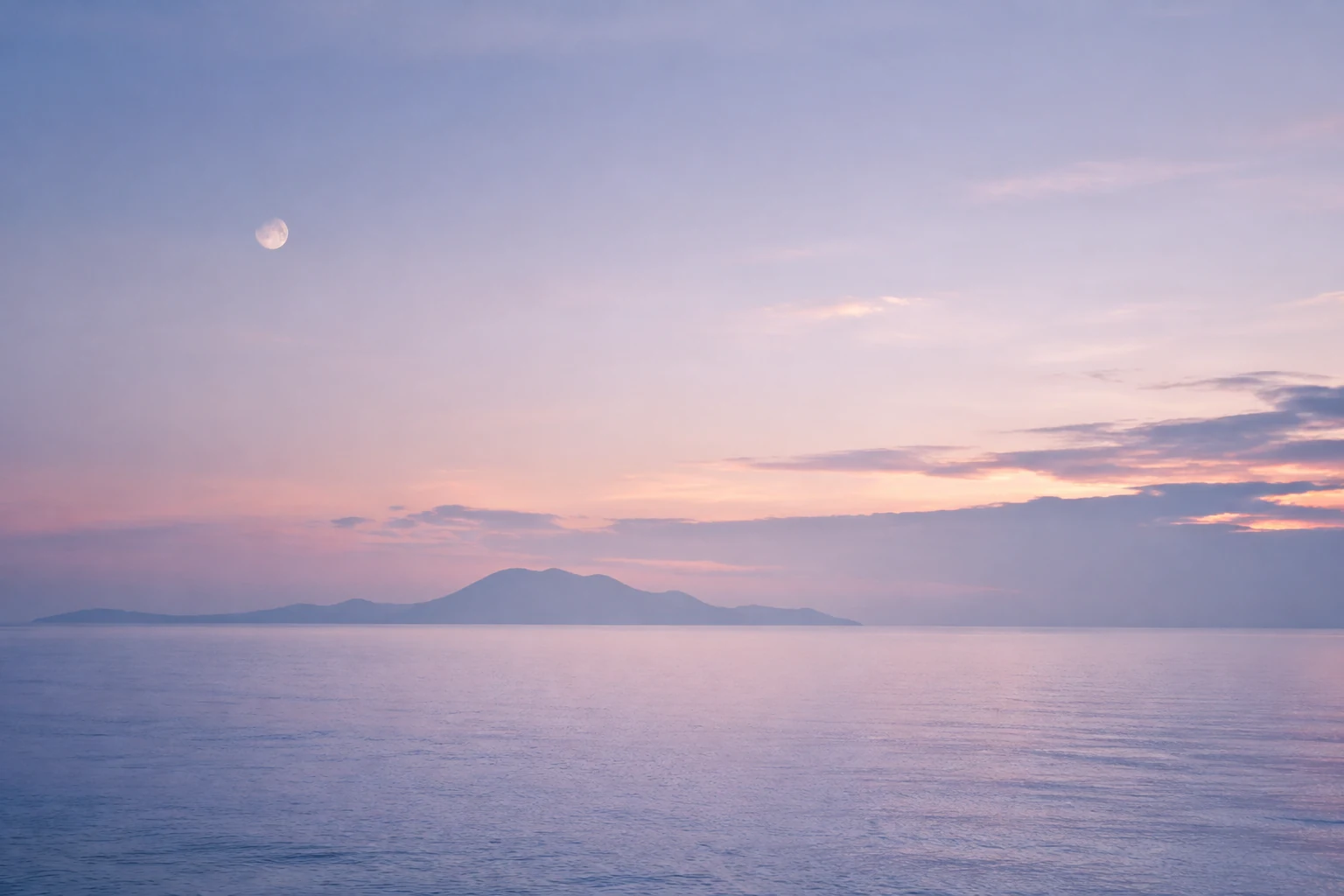 A fading moon over a lavender-blue dawn sea and a distant island
